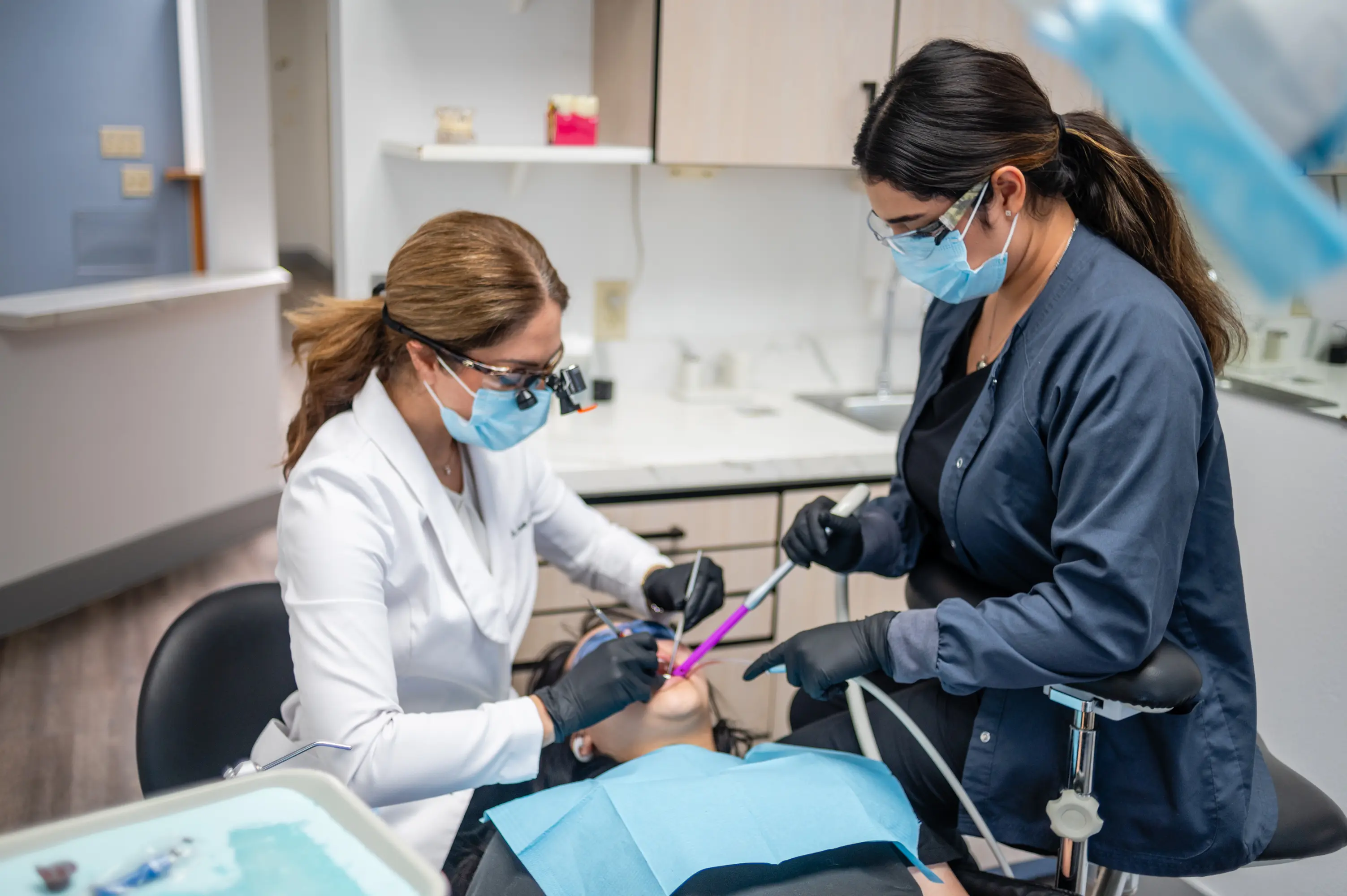 Two women in masks are working on a patient.