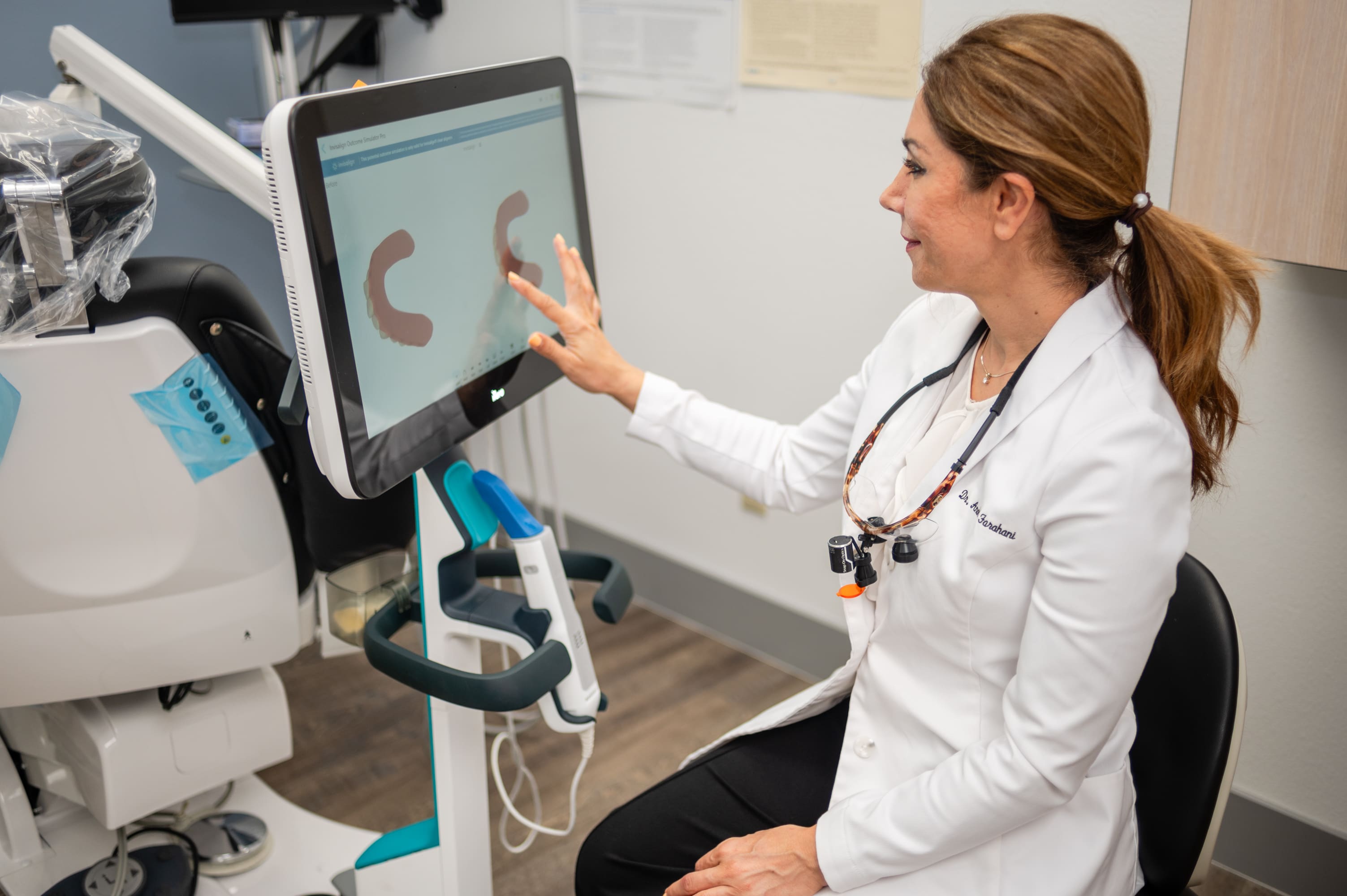 A woman in white lab coat pointing to an image on a computer screen.