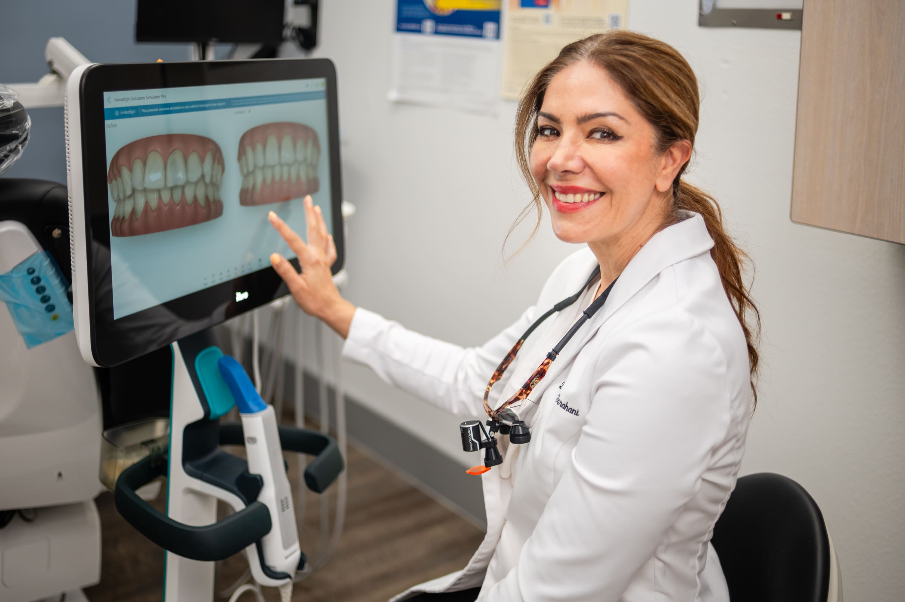 A woman in white shirt pointing to teeth on screen.