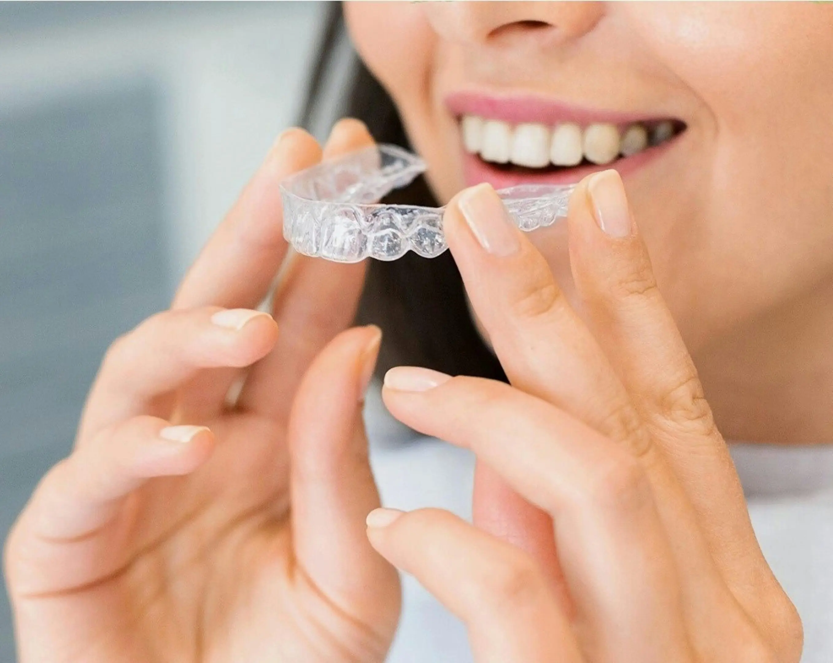 A woman holding an invisible aligner in her hand.